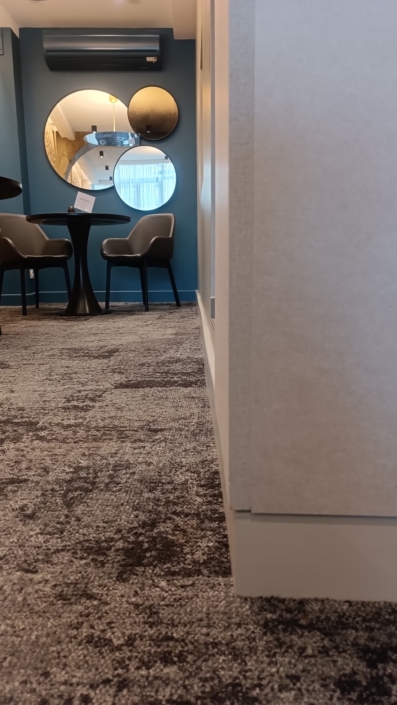 Une pièce moderne avec des murs bleus, des miroirs circulaires, une petite table noire et deux chaises grises sur un tapis à motifs crée un design élégant.