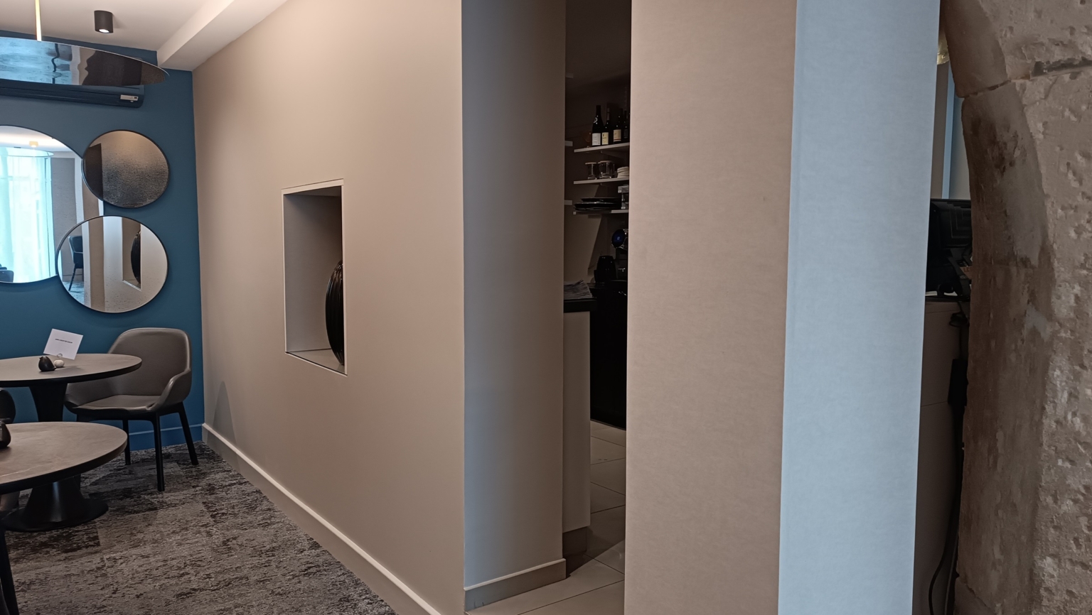 Salle à manger moderne avec miroirs circulaires, chaises grises et arche en pierre. Un éclairage subtil met en valeur l'espace tandis que des panneaux acoustiques sur les murs ajoutent une touche d'élégance et améliorent la qualité sonore.