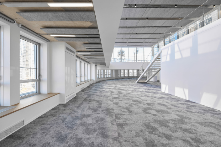 Intérieur spacieux et moderne avec de grandes fenêtres, un sol recouvert de moquette et un escalier menant à un niveau supérieur, évoquant l'ambiance raffinée d'un cadre acoustique.