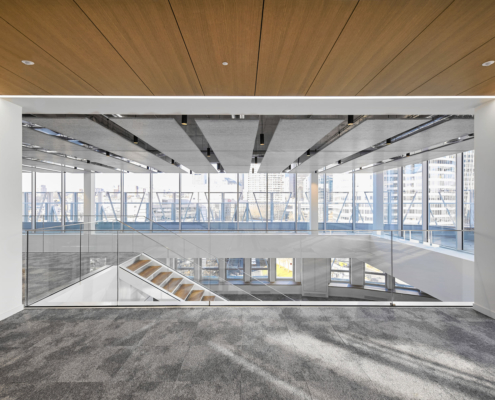 Modern office space with glass walls and an open staircase, featuring large windows offering city views and gymnasium-like acoustic enhancements to minimize noise.