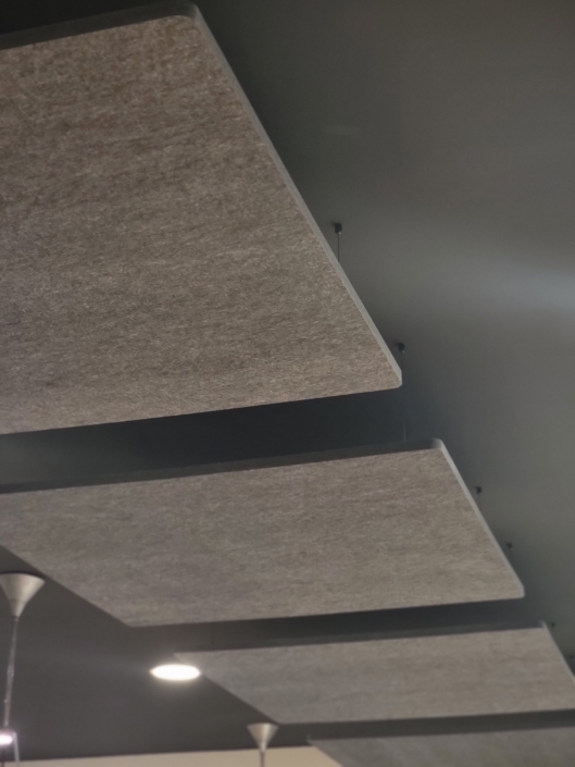 Des panneaux rectangulaires insonorisés suspendus à un plafond sombre créent une atmosphère sereine dans le restaurant acoustique, avec un luminaire élégant projetant une douce lueur.