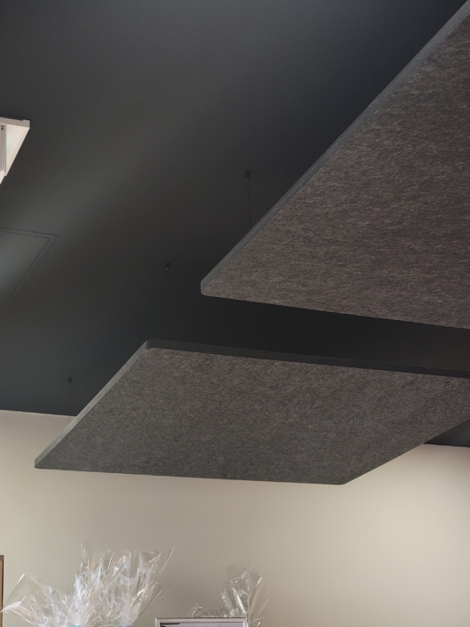 Un plafond orné de panneaux acoustiques rectangulaires suspendus surplombe un restaurant acoustique branché, où des articles emballés dans du plastique sont soigneusement disposés en dessous.