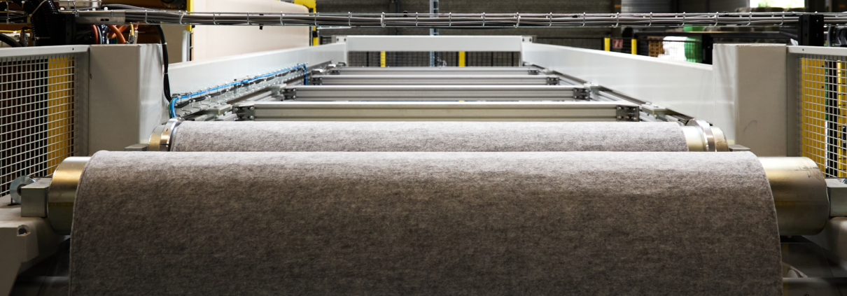 Grande machine industrielle avec un rouleau de tissu gris en cours de traitement dans une usine.