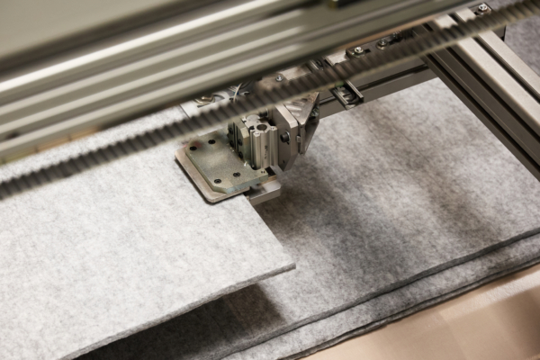 Close-up of an industrial sewing machine stitching together several layers of gray fabric.