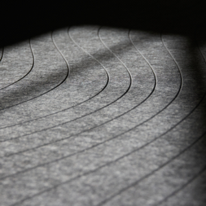 Lignes courbes et parallèles sur une surface grise texturée avec des motifs d'ombre et de lumière.