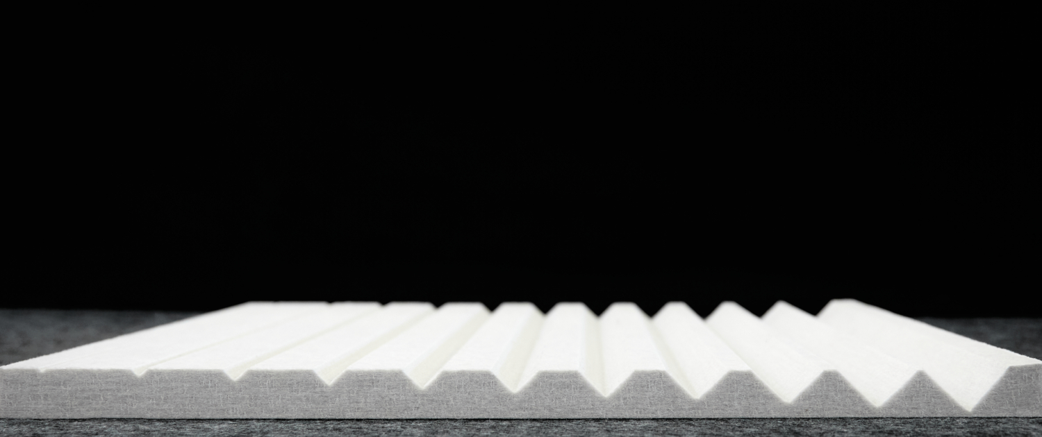 Un panneau de mousse blanc et strié est posé à plat sur une surface grise à fond noir.