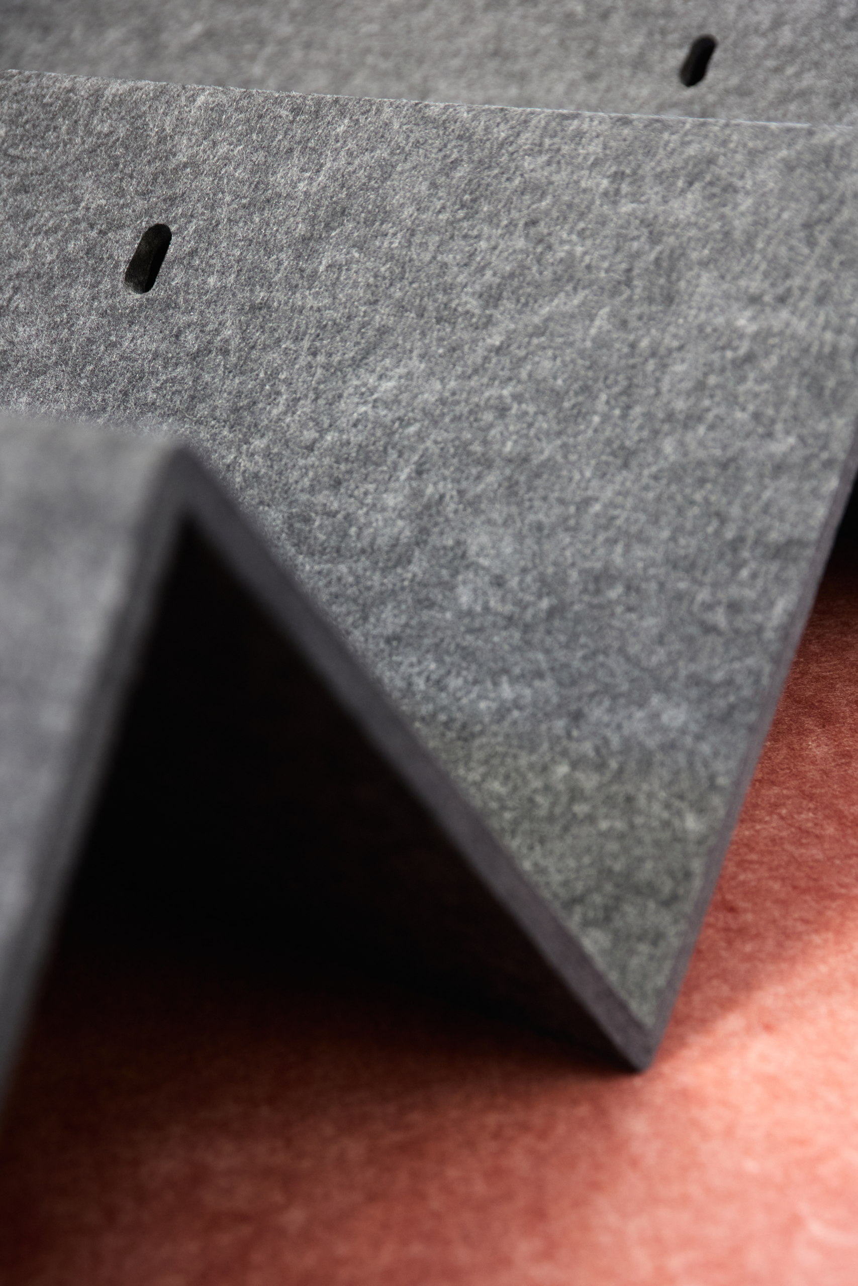 Gros plan sur des panneaux acoustiques gris, texturés, en zigzag, sur une surface brun-rouge.
