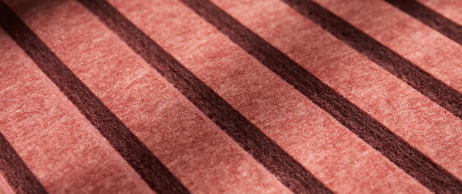 La lumière du soleil projette des ombres diagonales sur une surface rose avec des bandes sombres parallèles.