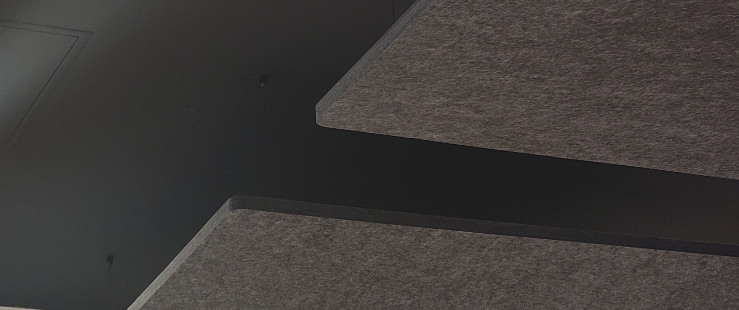 Dark acoustic panels suspended from a black ceiling above a beige wall and packed objects below.