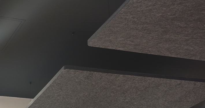 Panneaux acoustiques sombres suspendus à un plafond noir au-dessus d'un mur beige et d'objets emballés en dessous.