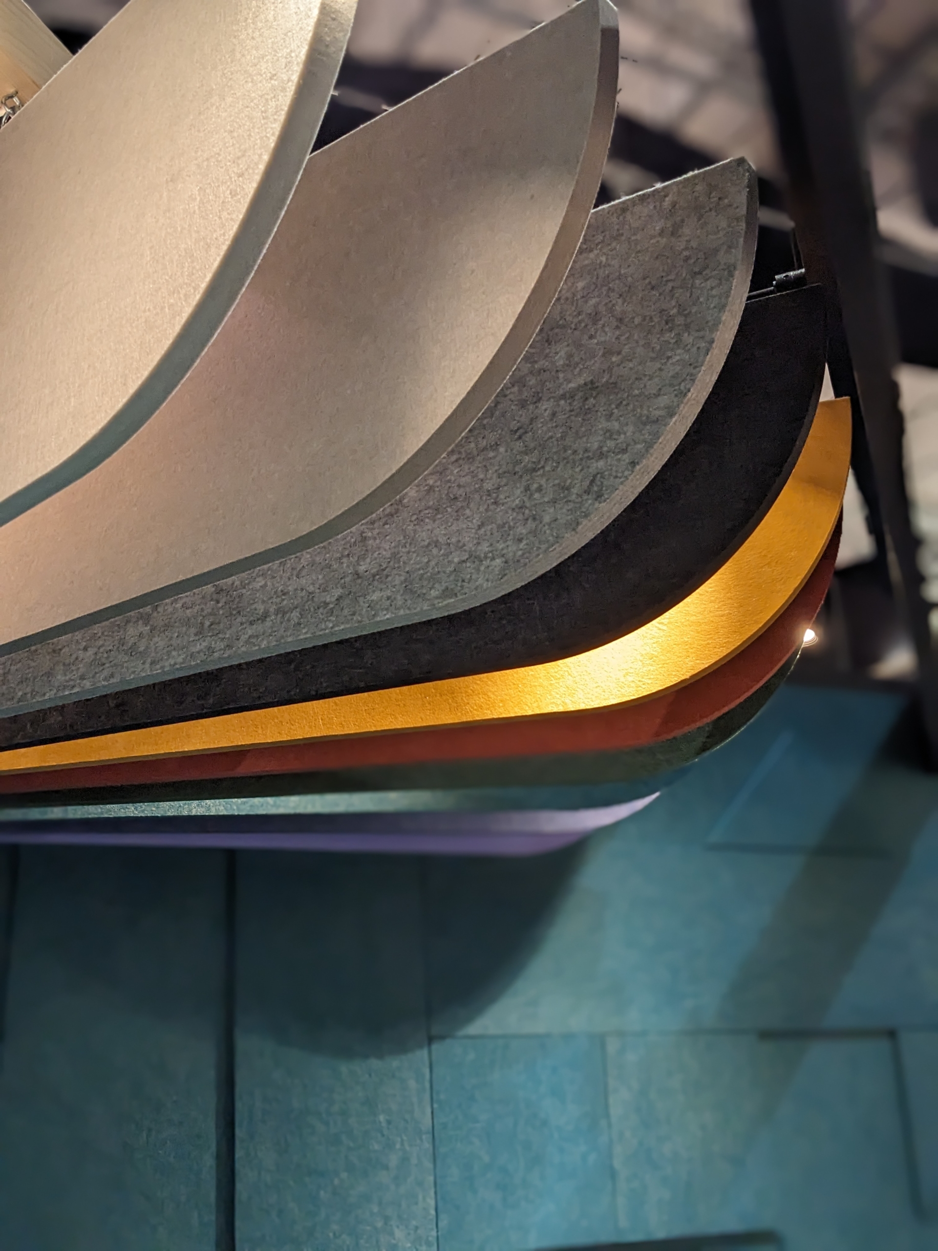 Des panneaux acoustiques courbes et superposés de différentes couleurs (gris, noir, or et marron) sont suspendus au plafond.