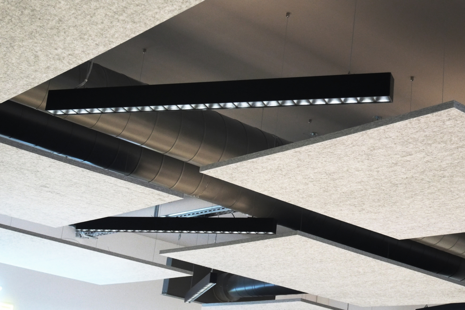 Black rectangular ceiling lights and large acoustic gymnasium panels, with exposed ducts above.