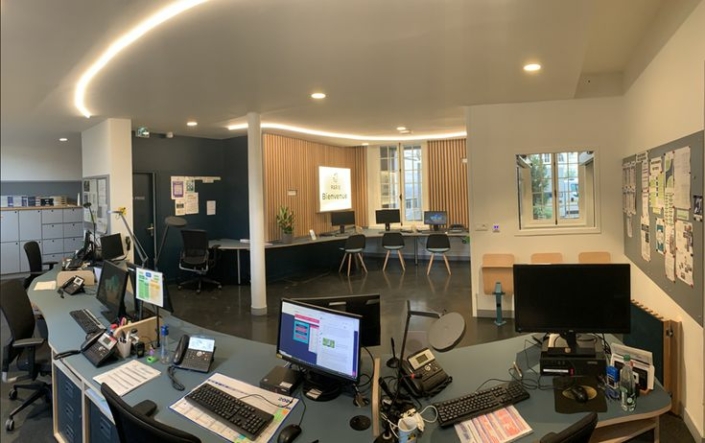 Una moderna area reception, dotata di scrivanie, computer, sedie, pannelli espositivi a parete e un cartello di benvenuto, integra elementi di design ispirati ai principi dell'acustica delle palestre per offrire uno spazio di lavoro più silenzioso e confortevole.