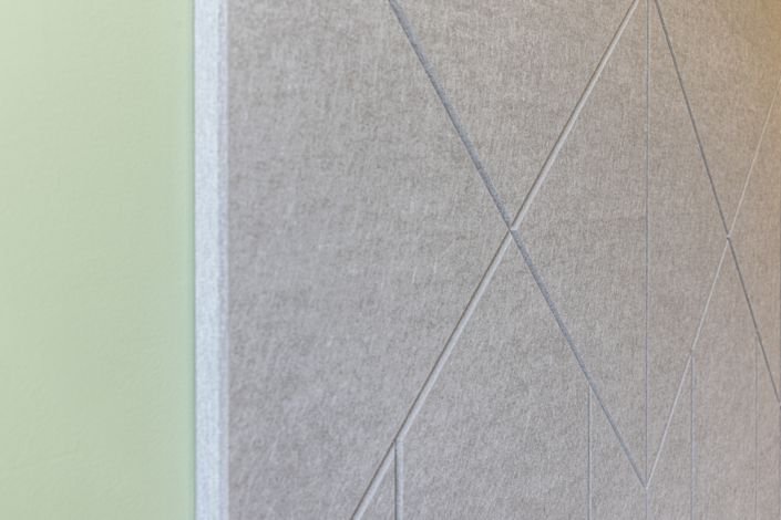Primo piano di una parete con una sezione verde chiaro e un pannello acustico grigio per palestra decorato con motivi geometrici.