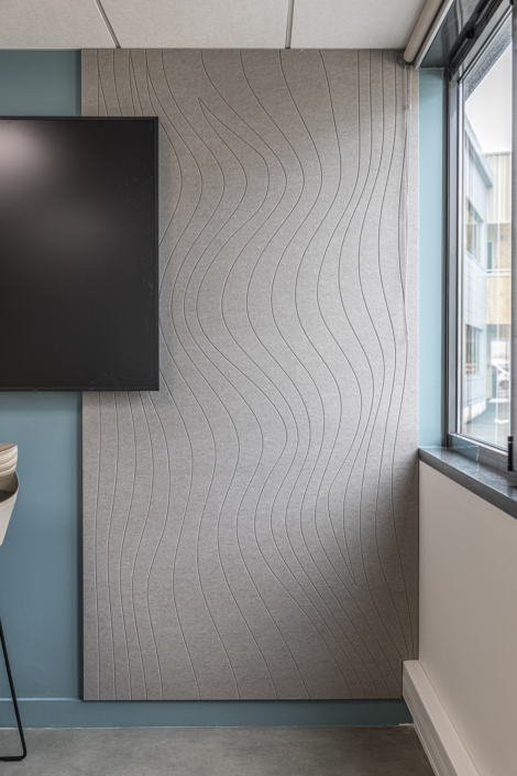 In questa stanza moderna, un pannello acustico grigio a parete, decorato con motivi ondulati, aggiunge un tocco di eleganza accanto al televisore e all'ampia finestra. Questo pannello trae ispirazione dal design acustico delle palestre per un controllo ottimale del suono.