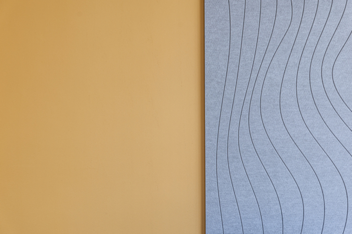 Una parete arancione accanto a un pannello grigio texturizzato decorato con linee ondulate; un design minimalista e moderno per la palestra, acusticamente ottimizzato.
