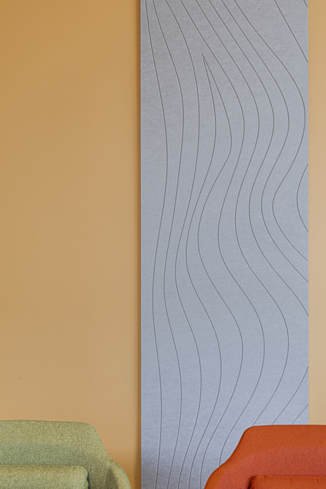 Due sedie colorate davanti a un grande pannello acustico grigio da palestra con motivi ondulati, appeso a una parete arancione.