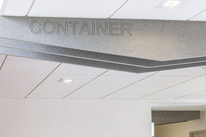 Pannelli a soffitto grigi con la scritta "CONTAINER" a caratteri cubitali; un design d'interni moderno e minimalista che incorpora elementi acustici tipici di una palestra.