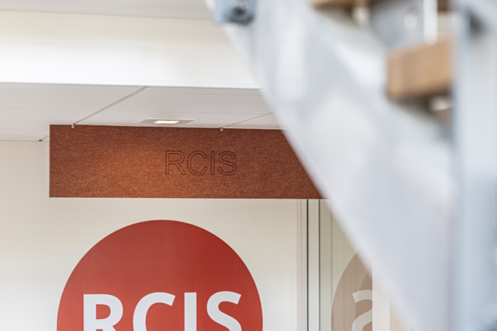 L'insegna "RCIS" è affissa a una parete, con parte di una scala visibile in primo piano, che offre uno scorcio della palestra acustica situata alle sue spalle.
