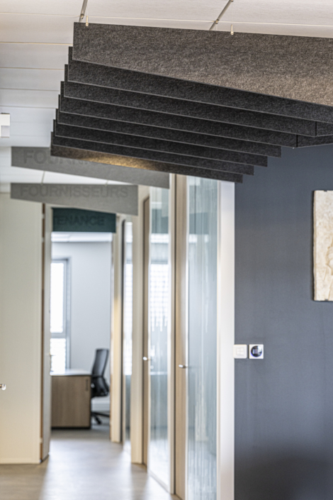 Corridoio di un ufficio moderno con porte a vetri, una sedia vuota e pannelli acustici neri sul soffitto, che ricordano il design acustico di una palestra per un controllo ottimale del suono.