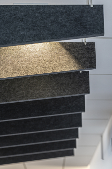 In questa palestra insonorizzata, pannelli acustici rettangolari sono sospesi al soffitto; uno di essi è illuminato da un faretto posizionato sopra.