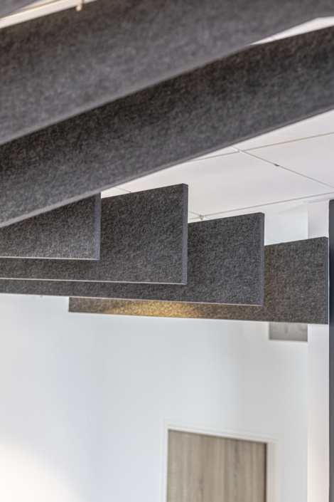 In un ambiente interno moderno e minimalista, pannelli acustici grigi sono sospesi a un soffitto bianco, creando un'atmosfera da palestra acustica che esalta sia lo stile che la qualità del suono.