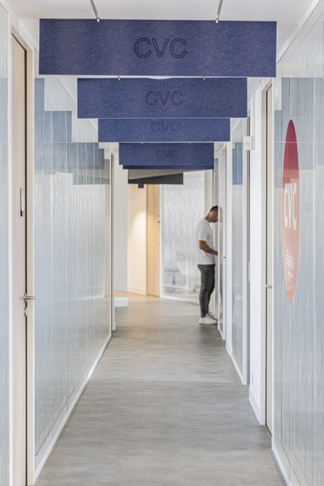 Un uomo si trova in un corridoio moderno, adornato da pannelli di climatizzazione sul soffitto e sulle pareti, al centro di una palestra dal design elegante e acusticamente ottimizzata, e guarda qualcosa.