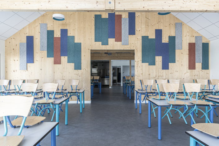 Aula moderna con pareti in legno, pannelli acustici colorati e file di sedie e tavoli vuoti.