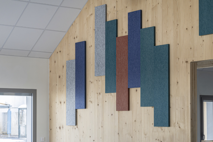Pannelli acustici rettangolari di diversi colori, fissati a una parete in legno in un ambiente interno moderno, ideali per migliorare l'acustica di una palestra.