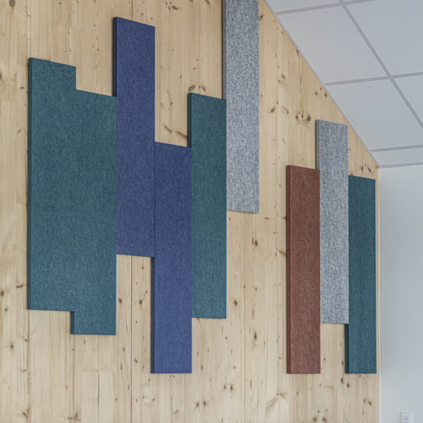 Des panneaux rectangulaires colorés, au design inspiré des gymnases, sont fixés sur un mur en bois au-dessus de chaises bleues et en bois, dans une pièce moderne.