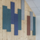 In una stanza moderna, pannelli rettangolari colorati, con un design ispirato alle palestre, sono fissati a una parete di legno sopra sedie blu e in legno.