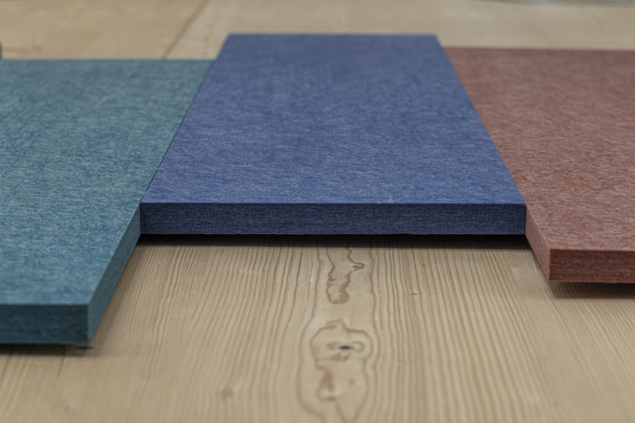 Tre pannelli rettangolari colorati – turchese, blu e rosso – sono disposti su una superficie di legno chiaro, richiamando i pannelli acustici dai colori vivaci delle palestre, pronti ad abbellire qualsiasi spazio sportivo migliorandone al contempo la qualità del suono.