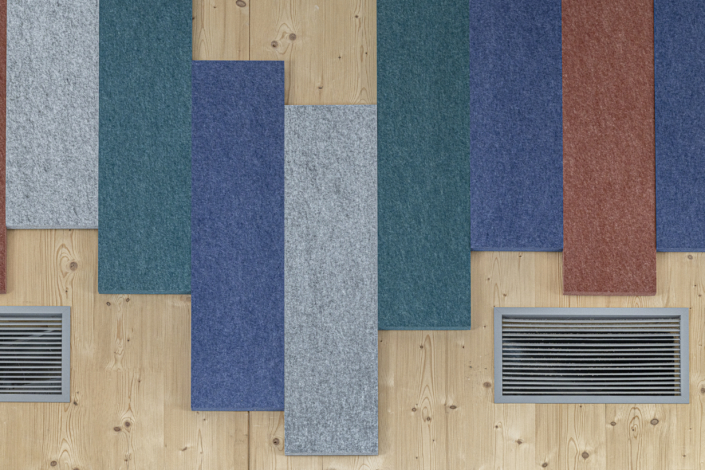 Pannelli in feltro colorato e due aperture di ventilazione su una parete in legno chiaro, disposte verticalmente, creano un design per la palestra ispirato all'acustica, che coniuga estetica e assorbimento acustico.