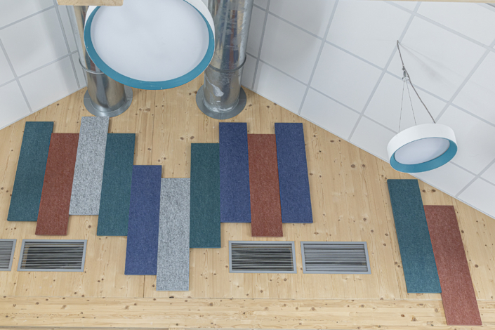 Il soffitto in legno, composto da pannelli rettangolari colorati, bocchette di ventilazione, due grandi lampade circolari e condotti a vista, conferisce alla palestra un aspetto dinamico e moderno, migliorandone al contempo le prestazioni acustiche.