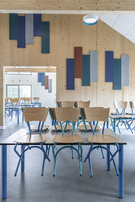 Aula moderna con sedie impilate sui tavoli, pareti in legno e pannelli fonoassorbenti colorati ispirati al design acustico delle palestre.