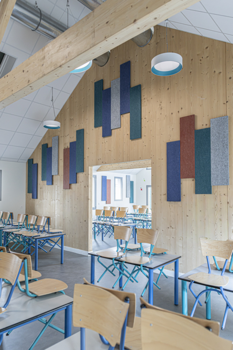 Aula con pareti in legno, dotate di pannelli colorati progettati per fornire un isolamento acustico di qualità "da palestra", con banchi e sedie vuoti impilati uno sull'altro.
