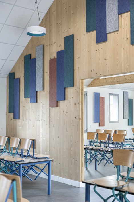 Un'aula moderna con pareti in legno, pannelli acustici colorati che ricordano quelli di una palestra, e sedie vuote disposte ordinatamente davanti ai banchi.